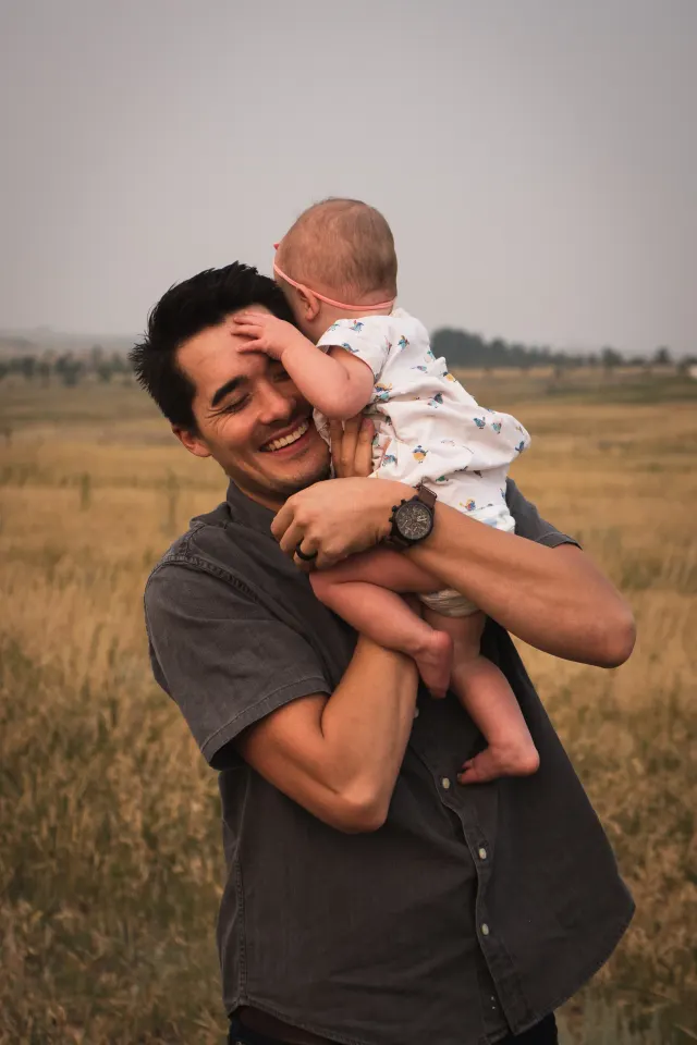A father carries his child through a sunlit field.